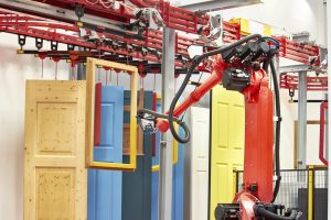 orange and black robotic arm spray painting doors and window frames in a construction warehouse, robotics in construction, tech outlook collaboration